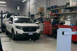 Back To School Car Maintenance in Thornton, CO At Alternative Auto Care. White Honda pickup truck inside a fully equipped auto repair bay next to tool cabinets